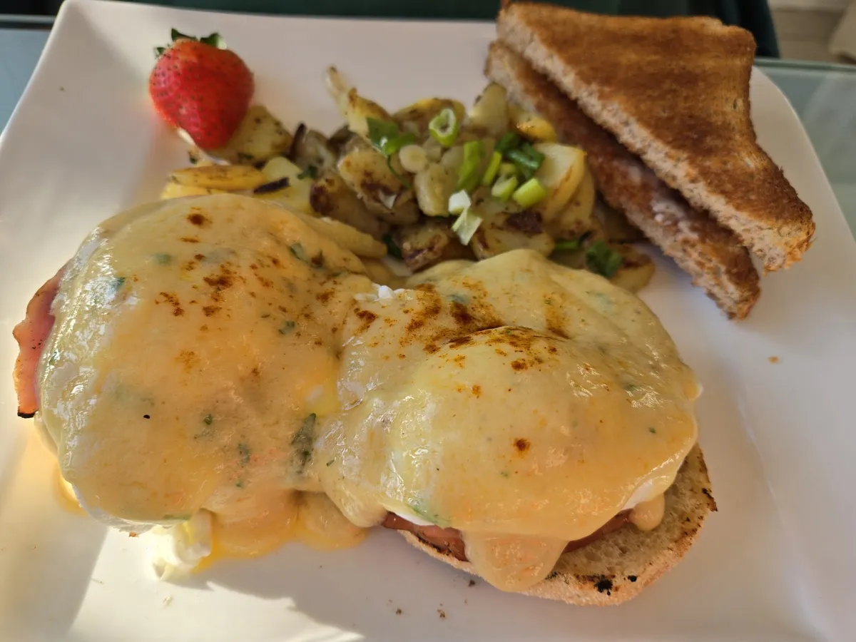 Eggs Benedict with potatoes, toast, and a strawberry